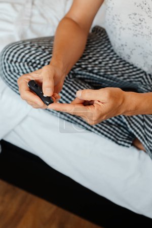 Téléchargez les photos : Gros plan d'un homme caucasien au lit sur le point de mesurer sa glycémie dans un glucomètre en lui piquant le doigt avec un doigt - en image libre de droit