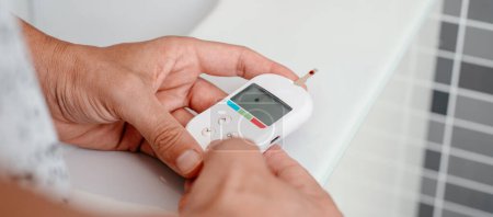 Photo for Closeup of a man measuring his blood glucose level in a glucose meter, in the bathroom, in a panoramic format to use as web banner or header - Royalty Free Image