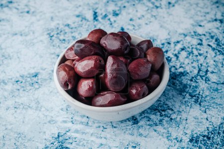Photo for A small white ceramic bowl with some kalamata olives placed on a stone surface - Royalty Free Image