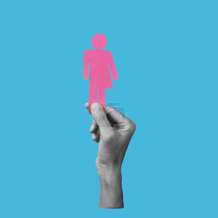 Photo for The hand of a man in black and white holding a pink gender neutral icon on a blue background - Royalty Free Image