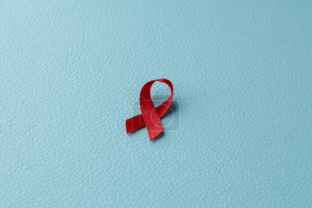 Photo for A red awareness ribbon, for the fight against AIDS, placed on a blue leatherette surface - Royalty Free Image