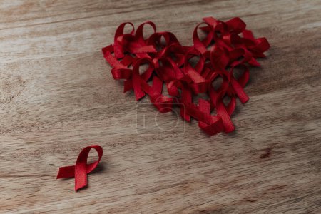 Photo for Some red awareness ribbons, for the fight against AIDS, forming a heart on a wooden table - Royalty Free Image