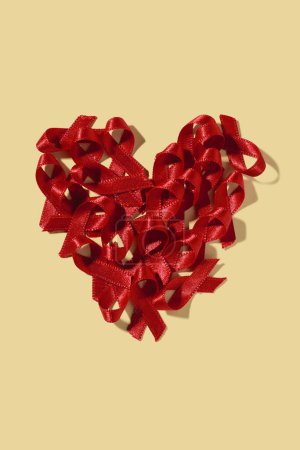 Téléchargez les photos : Quelques rubans rouges de sensibilisation, pour la lutte contre le sida, formant un cœur sur un fond jaune pâle - en image libre de droit