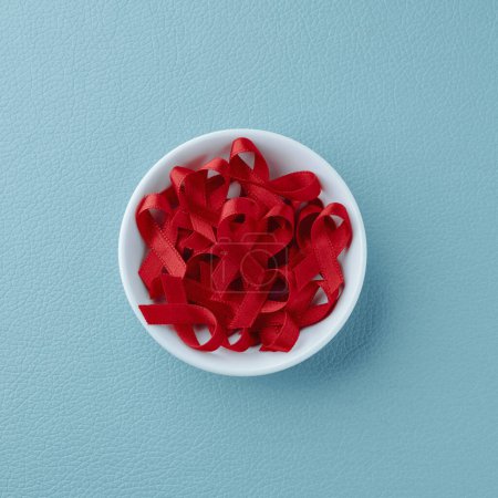 Photo for High angle view of a white ceramic bowl with some red awareness ribbons, for the fight against AIDS, on a blue leatherette surface - Royalty Free Image