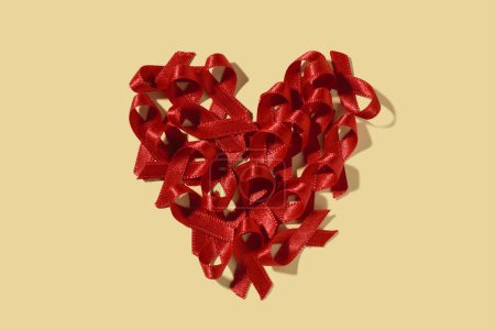 Photo for High angle view of some red awareness ribbons, for the fight against AIDS, arranged forming a heart on a yellow background - Royalty Free Image
