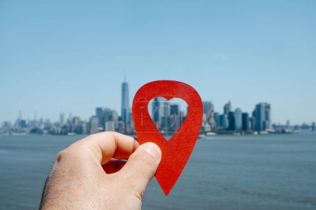Foto de La mano de un hombre sosteniendo un marcador rojo con un agujero en forma de corazón apuntando al Distrito Financiero, en Manhattan, Nueva York, Estados Unidos, como se ve desde la bahía, en primer plano - Imagen libre de derechos