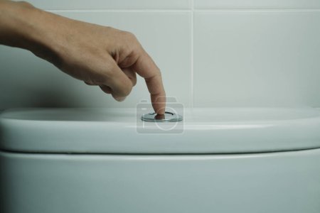 Foto de Un hombre está a punto de tirar el inodoro, presionando el botón, en un baño de azulejos después de usarlo - Imagen libre de derechos