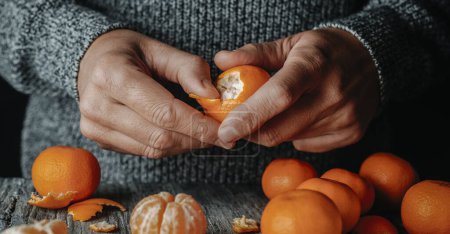 a man, wearing a gray sweater, peeling a tangerine on a gray rustic wooden table, in a panoramic format to use as web banner or header