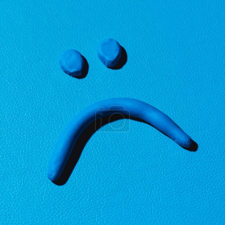Foto de Primer plano de una cara triste hecha con arcilla de modelado azul sobre un fondo de cuero azul - Imagen libre de derechos
