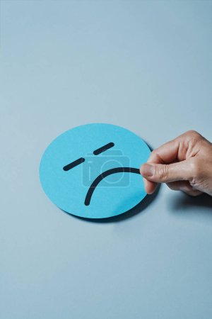 Photo for A man attaches a sad mouth to a blue cardboard face against a gray background - Royalty Free Image