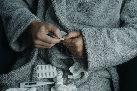 Foto de Primer plano de un hombre enfermo en casa, con una túnica gris cálida, rodeado de tejidos usados, a punto de tomar una píldora - Imagen libre de derechos