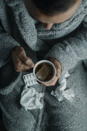 Foto de Vista de ángulo alto de un hombre enfermo en casa, con una túnica gris esponjosa de la casa, calentándose con una taza de té caliente de hierbas - Imagen libre de derechos