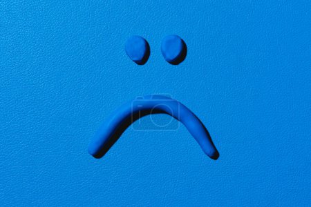 Photo for A sad face made with blue modelling clay on a blue background - Royalty Free Image
