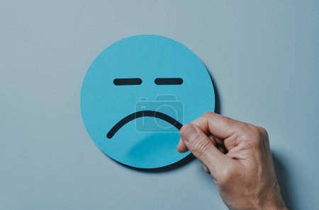 Photo for High angle view of a man attaching a sad mouth to a blue paper face on a gray background - Royalty Free Image