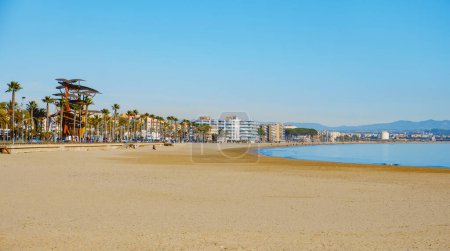 Foto de Vilaseca, España - 26 de diciembre de 2023: Una vista de la playa de La Pineda y su paseo marítimo, en Vilaseca, España, en un día soleado de invierno. La Pineda es un complejo costero en el mar Mediterráneo popular entre los lugareños - Imagen libre de derechos