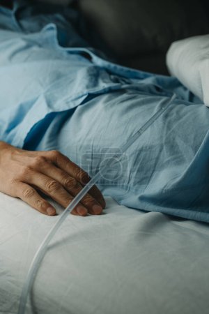 closeup of a man, lying face up in bed, in a blue pajamas, wearing a urinary catheterization