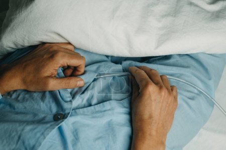 Photo for High ahgle view of a man, wearing a blue pajamas, handling his urinary catheterization lying in bed - Royalty Free Image