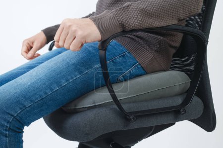 Téléchargez les photos : Gros plan d'un homme utilisant un coussin annulaire gonflable pour s'asseoir sur une chaise de bureau - en image libre de droit