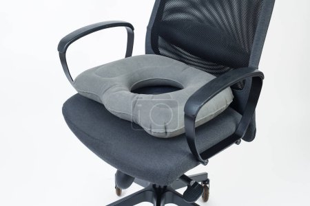 un coussin d'anneau gonflable gris placé sur une chaise de bureau, sur un fond blanc