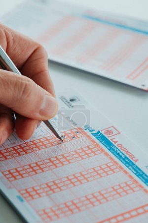 Photo for Barcelona, Spain - February 8, 2024: A man checks some checkboxes from a La Quiniela ticket, a sports betting game consisting of guessing the winner of fifteen football matches from the Spanish league - Royalty Free Image