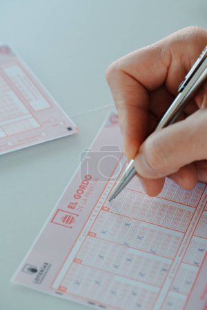 Téléchargez les photos : Barcelone, Espagne - 13 février 2024 : Un homme vérifie quelques chiffres dans les cases à cocher d'un billet de loterie El Gordo de la Primitiva avec un stylo. El Gordo est une loterie populaire en Espagne - en image libre de droit