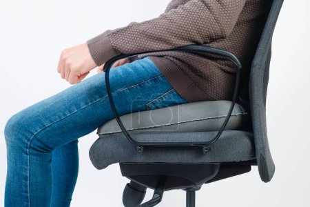 a caucasian man wearing casual clothes uses an inflatable ring cushion to seat on an office chair
