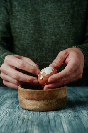 Photo for Closeup of a man peeling a brown boiled egg at a rustic gray wooden table - Royalty Free Image