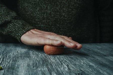 Photo for Closeup of a man rolling a hard-boiled egg against the table to remove its shell - Royalty Free Image