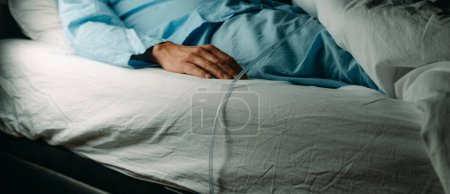 un hombre, en un pijama azul, lleva un cateterismo urinario mientras está acostado boca arriba en la cama, en un formato panorámico para usar como banner web