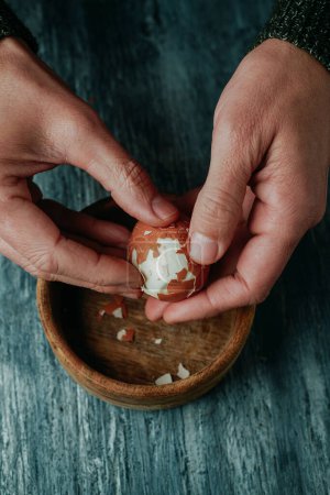 Photo for A man is peeling a hard-boiled egg at a rustic gray wooden table - Royalty Free Image
