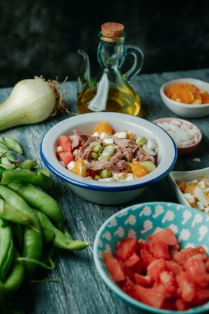 Téléchargez les photos : Une assiette avec une salade espagnole de fèves, typique de l'andalousie, avec tomate, oignon, oeuf bouilli, thon et orange, sur une table en bois gris rustique - en image libre de droit