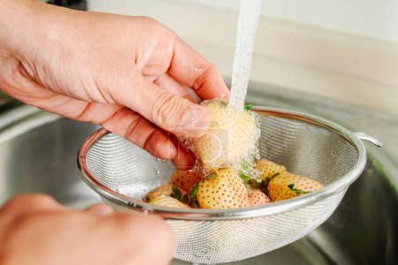 a man rinses some pineberries in a colander under the running water of the kitchen tap