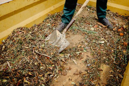 a man use a shovel to take out some plant remains from a large container for plant debris