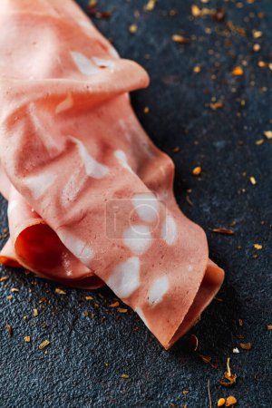 Photo for Closeup of a slice of mortadella on a dark textured surface - Royalty Free Image