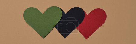 three hearts with the colors of the black liberation flag, green, black and red, on a brown background, in a panoramic format to use as web banner