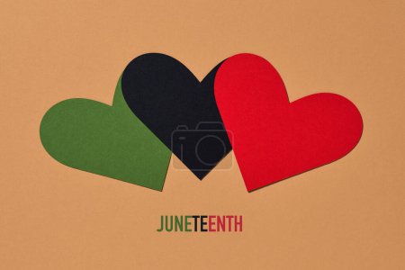 Téléchargez les photos : Three hearts with the colors of the black liberation flag, green, black and red, and the the text juneteenth on a brown background - en image libre de droit