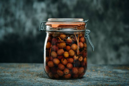 some marinated spanish arbequina olives in a mason jar, on a rustic gray wooden table
