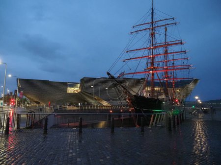 Photo for DUNDEE, UK - SEPTEMBER 13, 2023: RRS Discovery steamship for antarctic research in front of the Victoria and Albert museum at night - Royalty Free Image