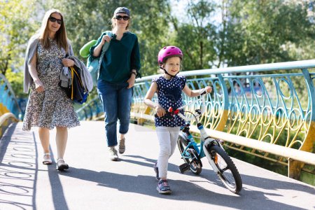 Photo for Young women and little girl with bicycle walking in park. Leisure time with family members. - Royalty Free Image