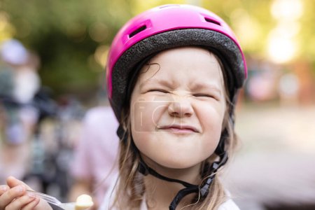 Photo for Cute young girl in helmet eating ice cream and making funny face - Royalty Free Image