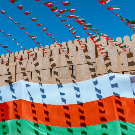 Téléchargez les photos : Drapeau national d'Oman pendant la fête de l'indépendance. Architecture médiévale traditionnelle à Nizwa, Oman. - en image libre de droit