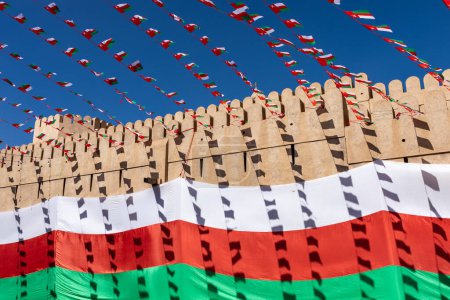 Téléchargez les photos : Drapeau national d'Oman pendant la fête de l'indépendance. Architecture médiévale traditionnelle à Nizwa, Oman. - en image libre de droit