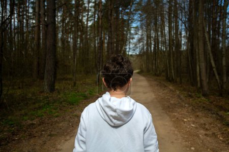 Foto de Adolescente en una sudadera con capucha blanca caminando en el bosque de primavera - Imagen libre de derechos