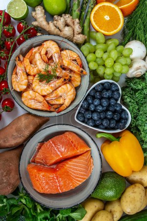 Photo for Shrimps, salmon fillet and fresh vegetables and fruits arranged around it, top view - Royalty Free Image