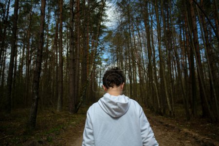 Téléchargez les photos : Adolescent dans un sweat à capuche blanc marchant dans la forêt de printemps - en image libre de droit