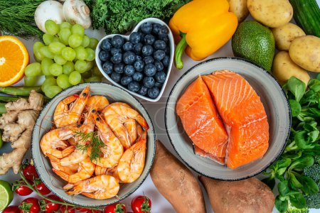 Photo for Shrimps, salmon fillet and fresh vegetables and fruits arranged around it - Royalty Free Image