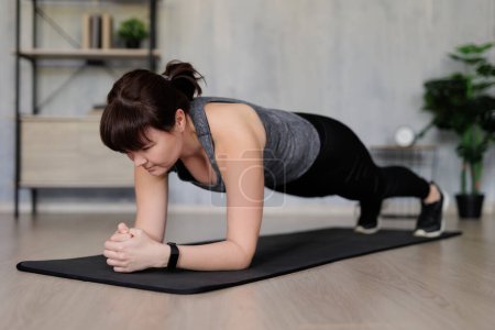 Photo for Young woman doing fitness exercises on yoga mat at home - Royalty Free Image