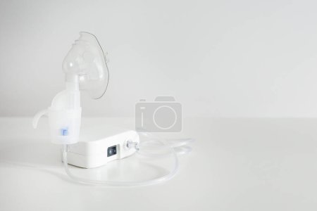 Medical equipment for inhalation with respiratory mask on white table with copyspace