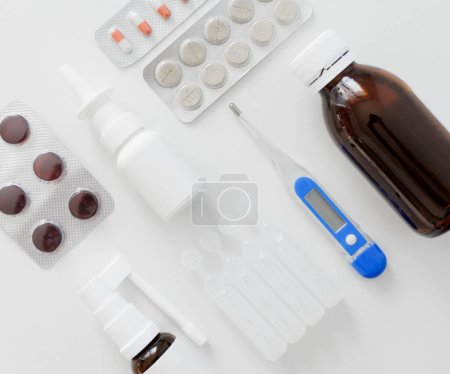 Photo for Top view of digital thermometer, nasal spray, pills and spray for the throat on white table - Royalty Free Image