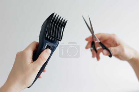 Close up of female hands holding hair clipper and scissors on white